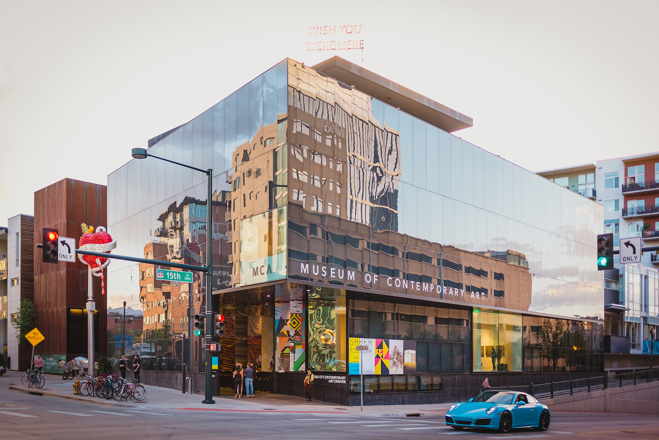 Exterior shot of the MCA Denver during the day. The surrounding ubran landscape is reflected in the museum's dark glass walls. 