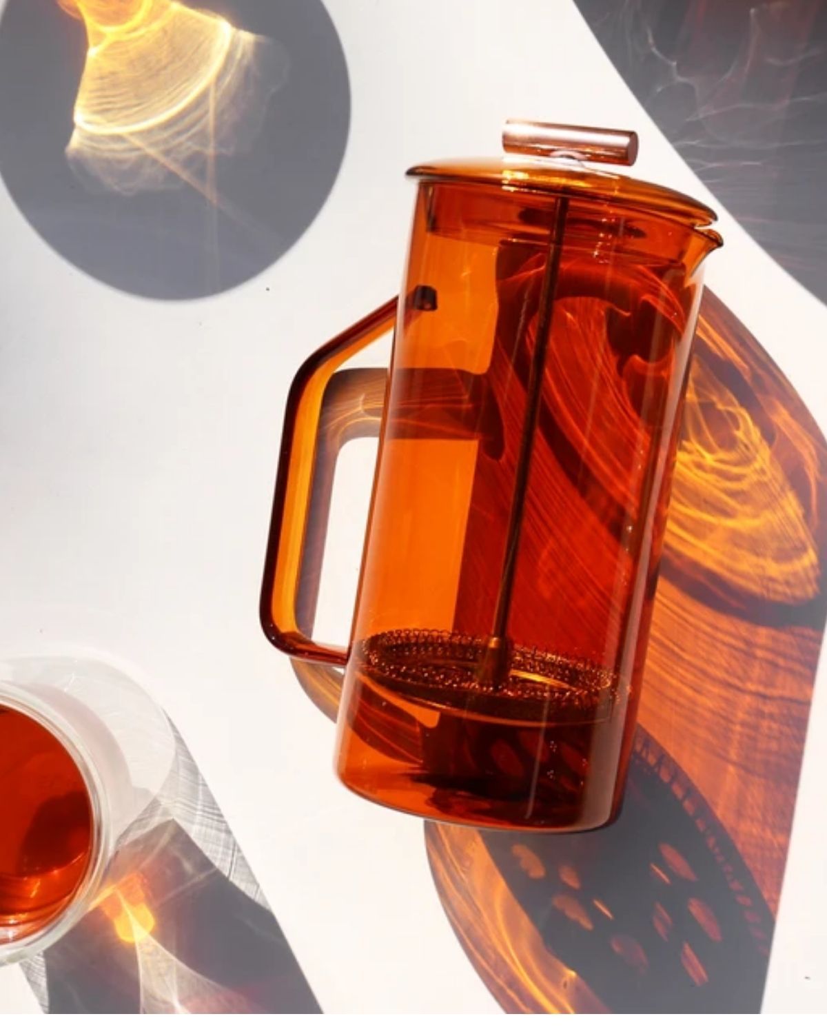 an orange glass french press, laying on a table in direct sunlight. 