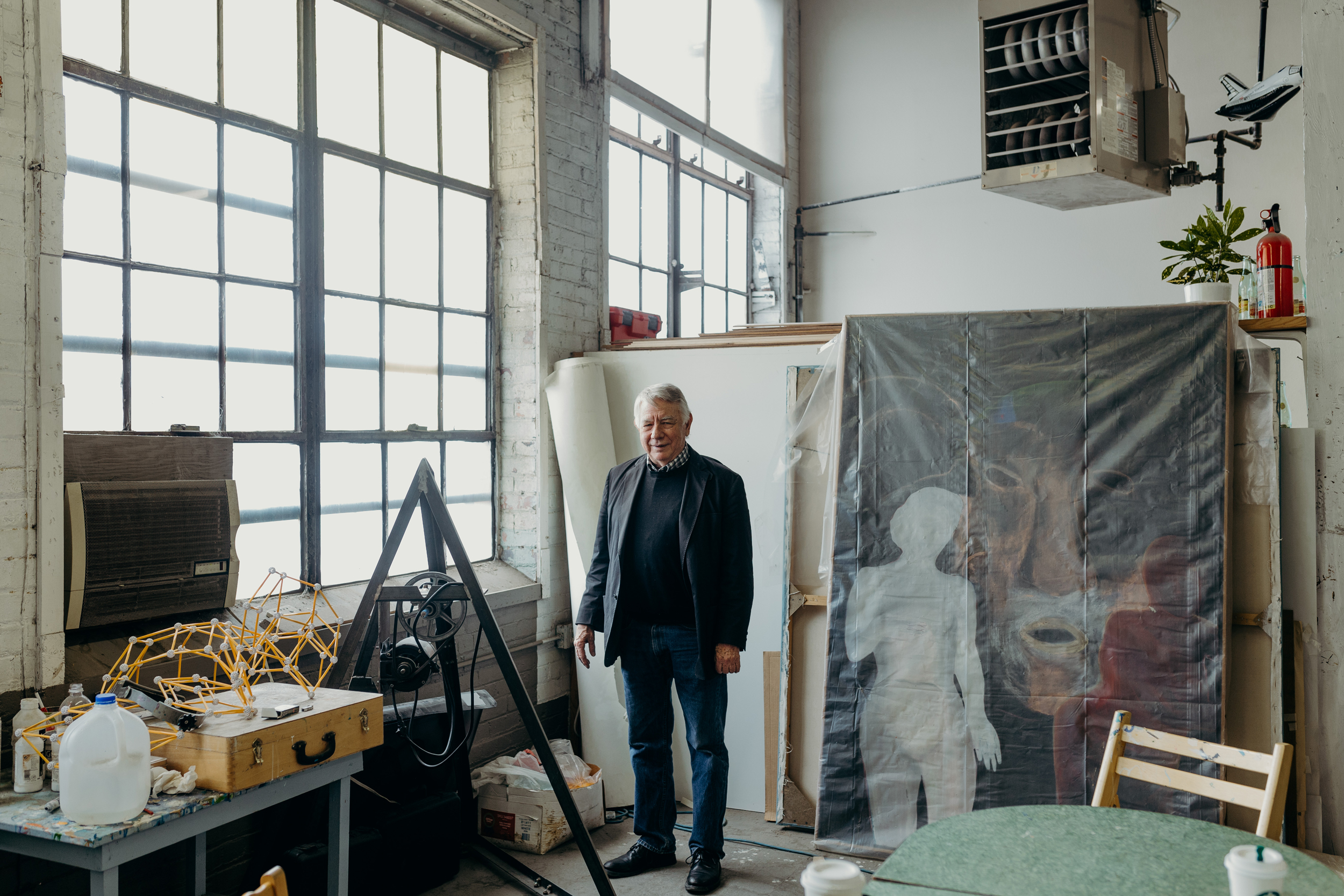 Clark richert stands in front of several paintings that are wrapped in plastic. 