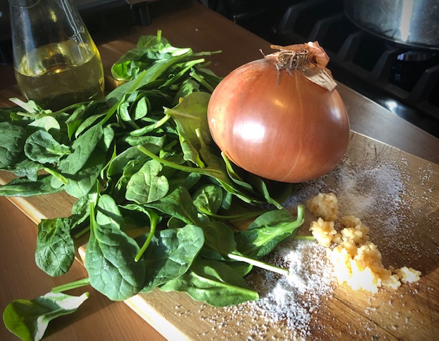 Spinach leaves on a cutting board with onion, salt, and minced garlic. 