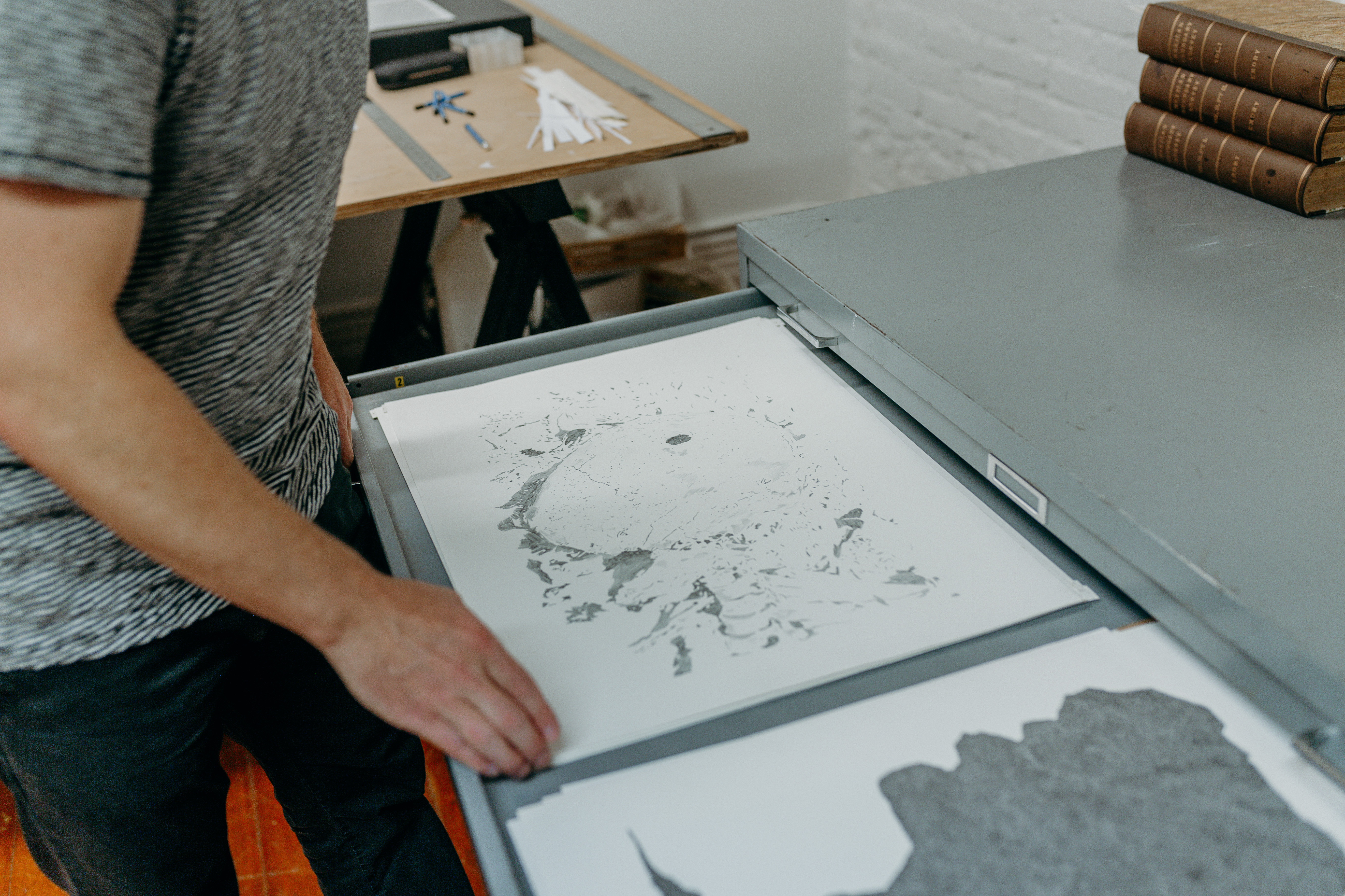 Chris Oatey going through a filing cabinet filled with abstract artworks of his. 