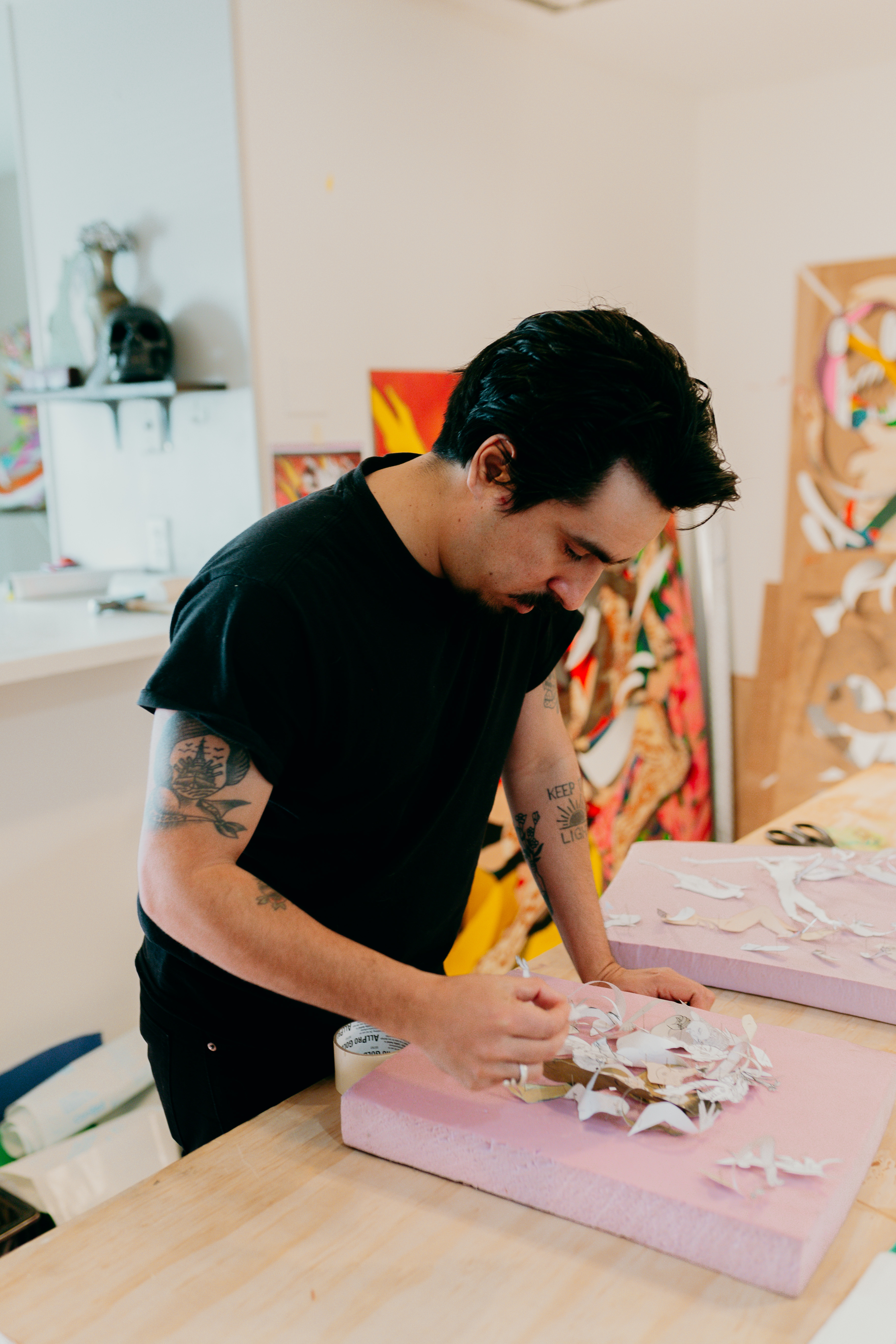 Candid shot of a man working in a studio surrounded by wood panel artworks and styrofoam .