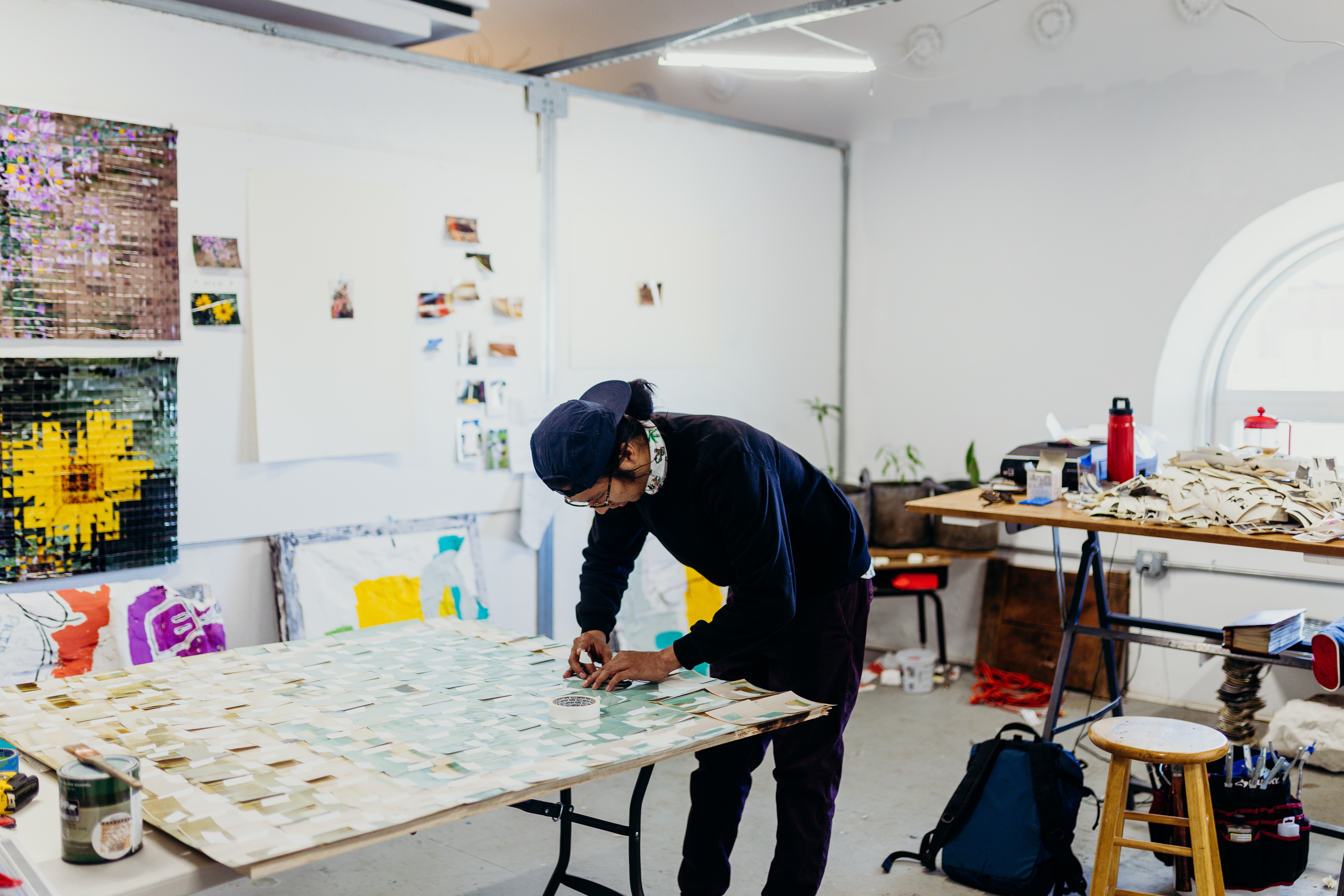 Candid shot of George P. Perez working in his studio. He is hunched over a table taping photographs down.