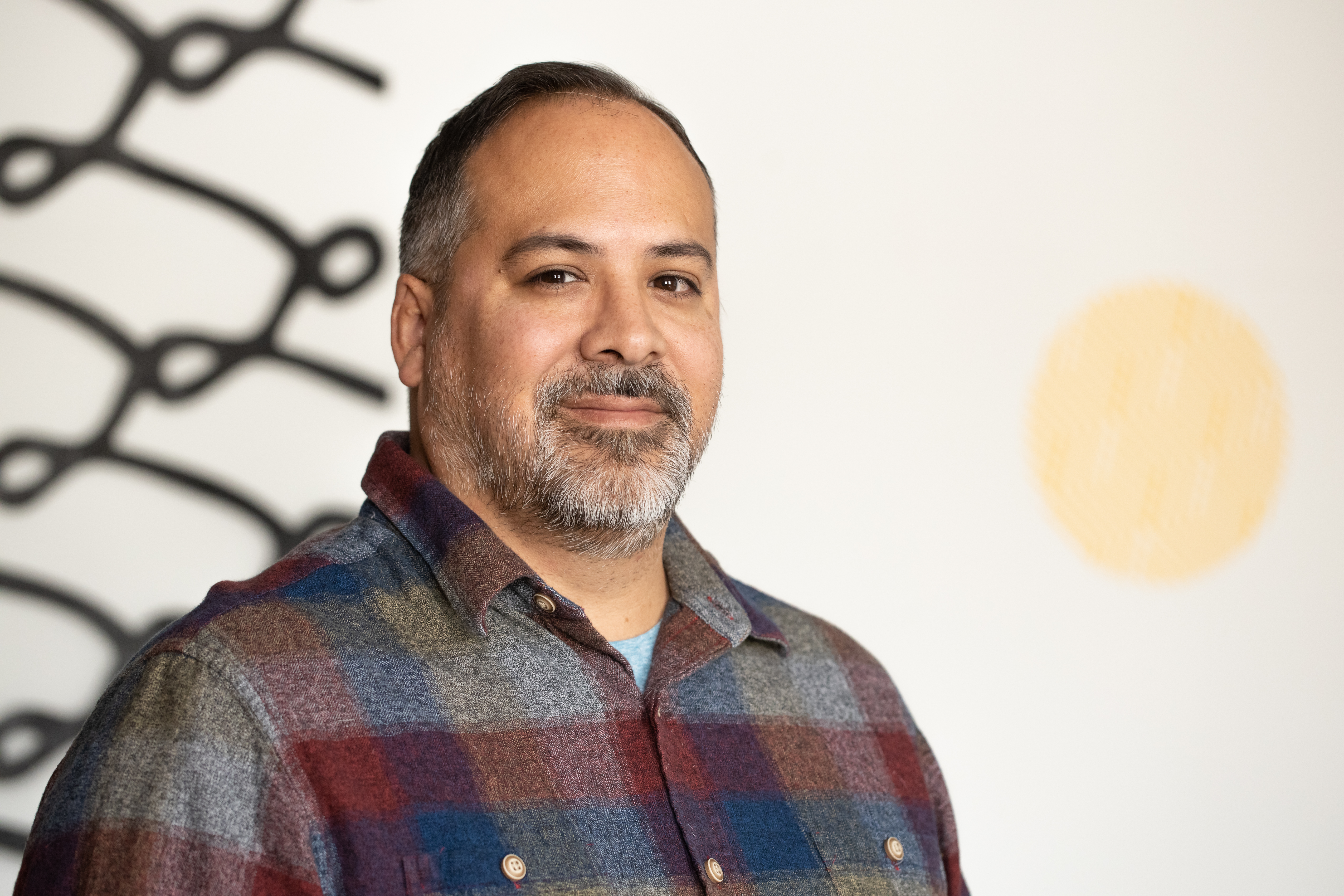 Portrait of Jaime Carrejo. He is wearing a plaid button up and smiles softly into the camera.