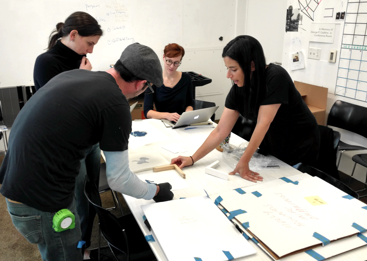 A curatorial team works on framing several artworks. 