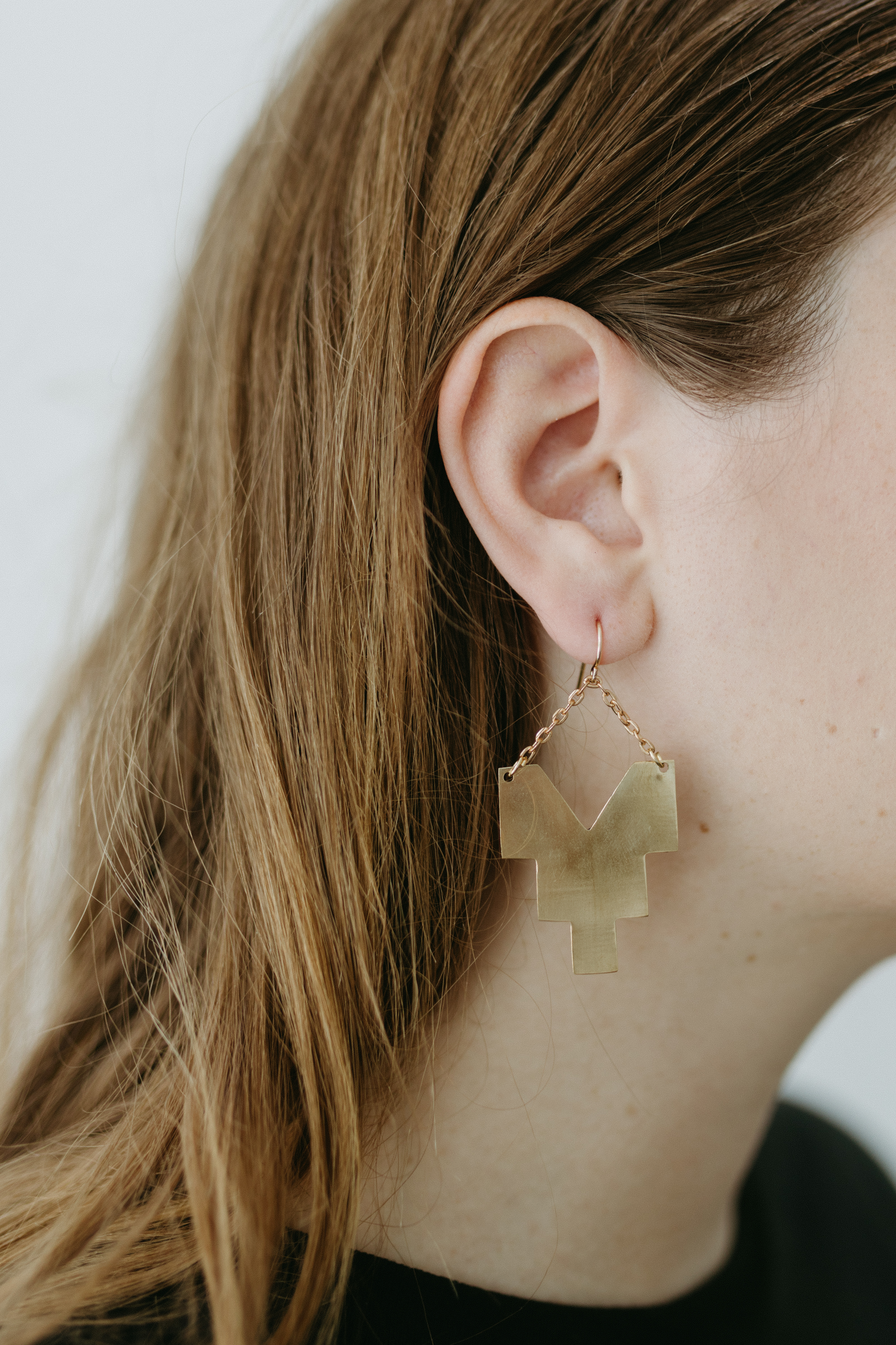 A woman models a golden earring. It is an abstract shape resembling an upside down step pyramid.