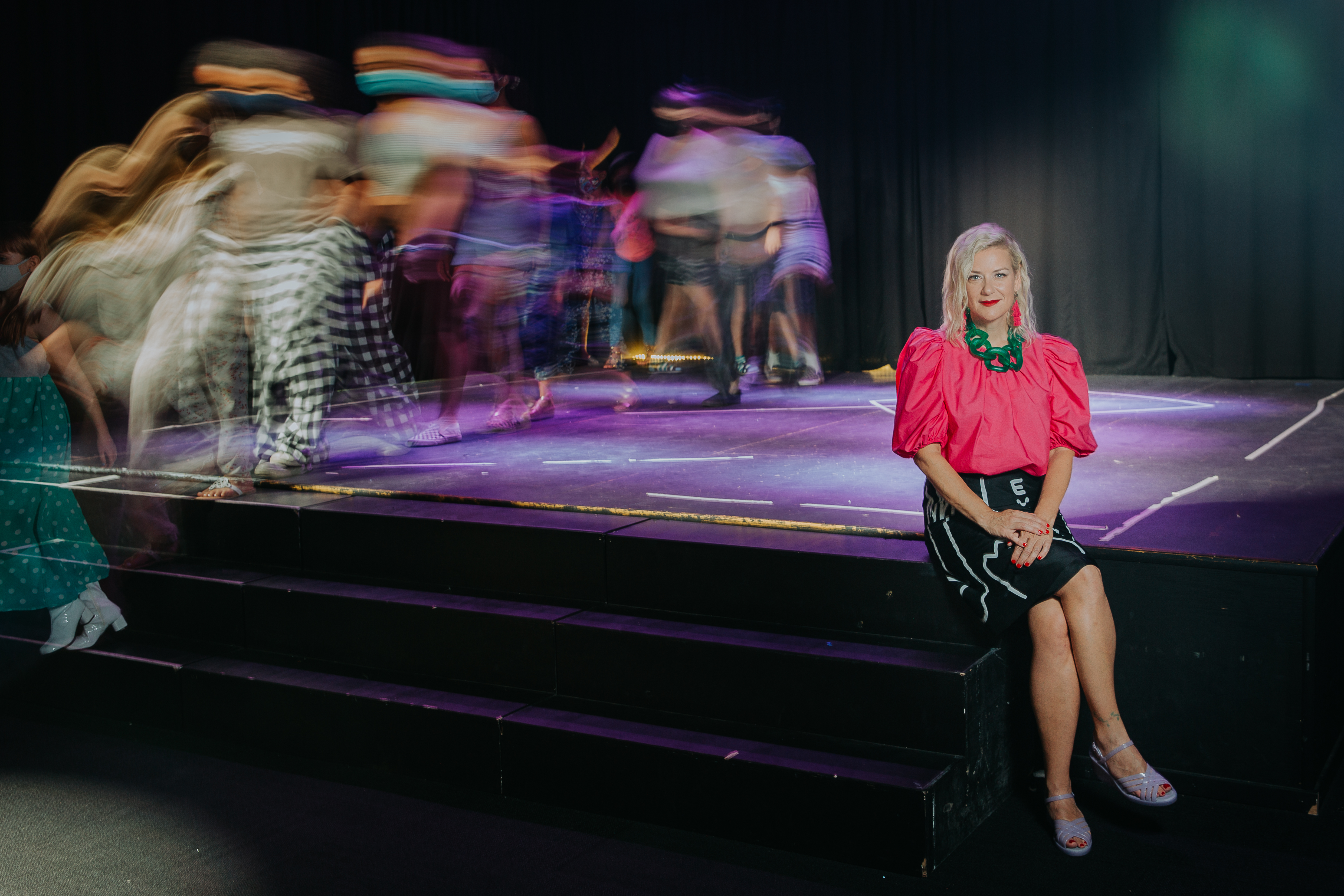 Photo of Skye Barker Maa on a stage with blurred image of students walking off the stage in the background