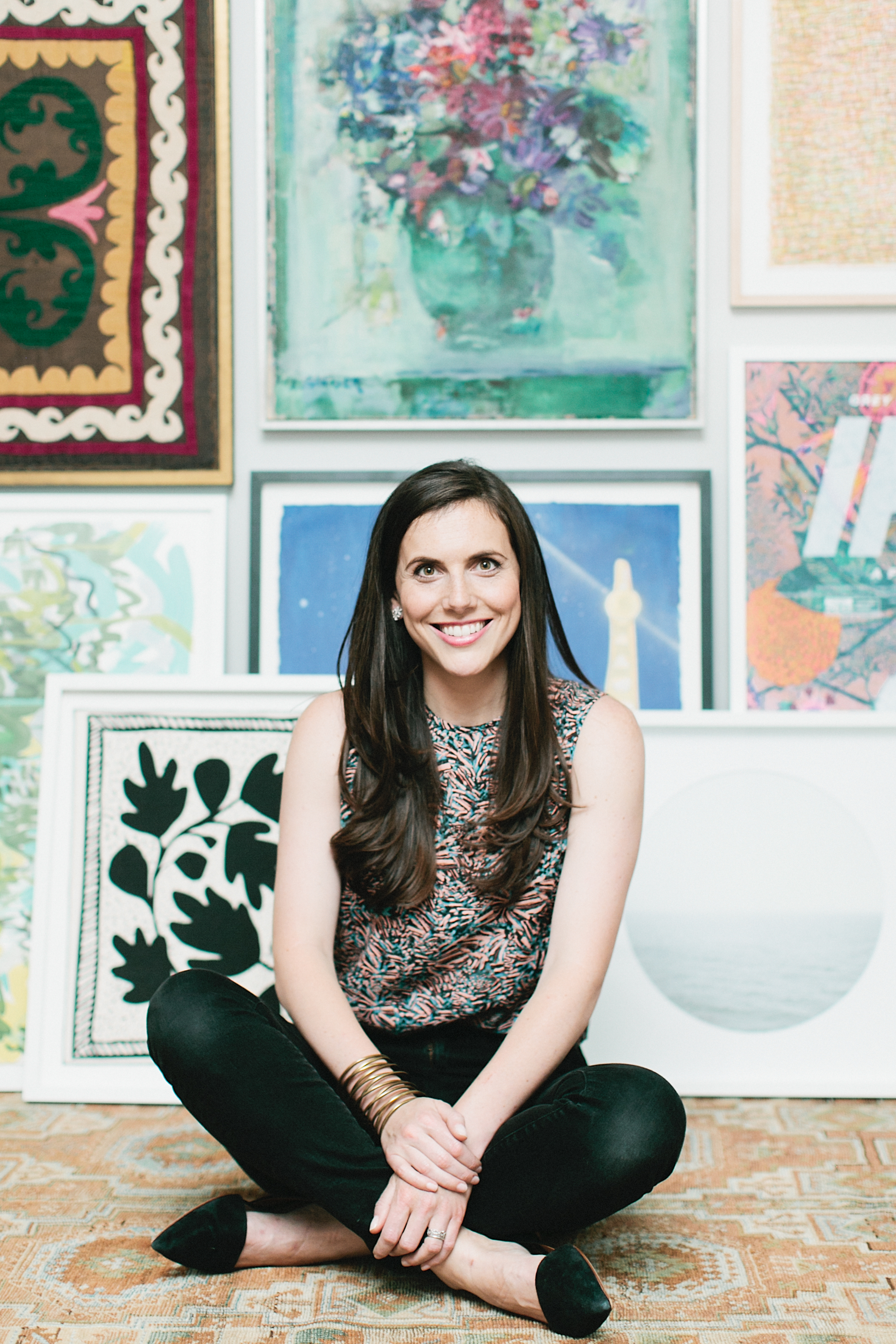 A woman sits cross legged on the floor in front of several artworks