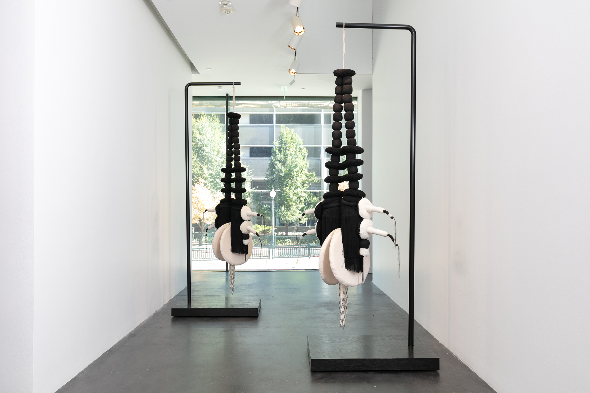 Two large soft sculptures that look like dangly earrings, hanging in a gallery.