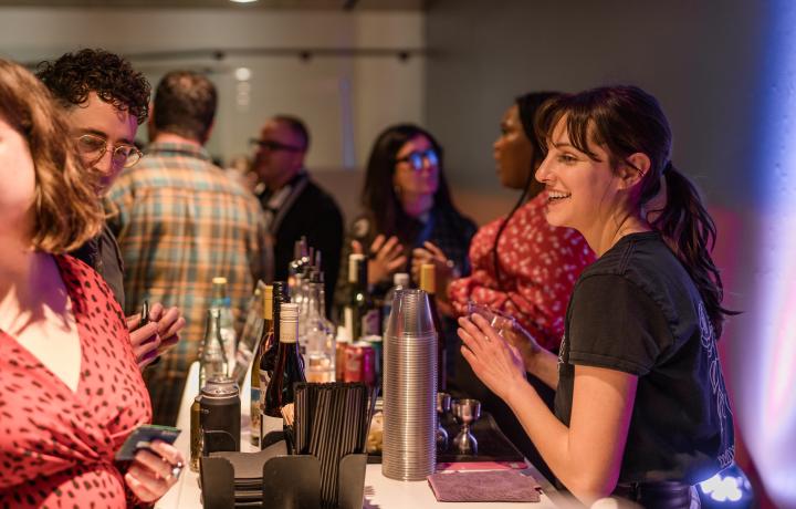 Bartender smiling surrounded by people.